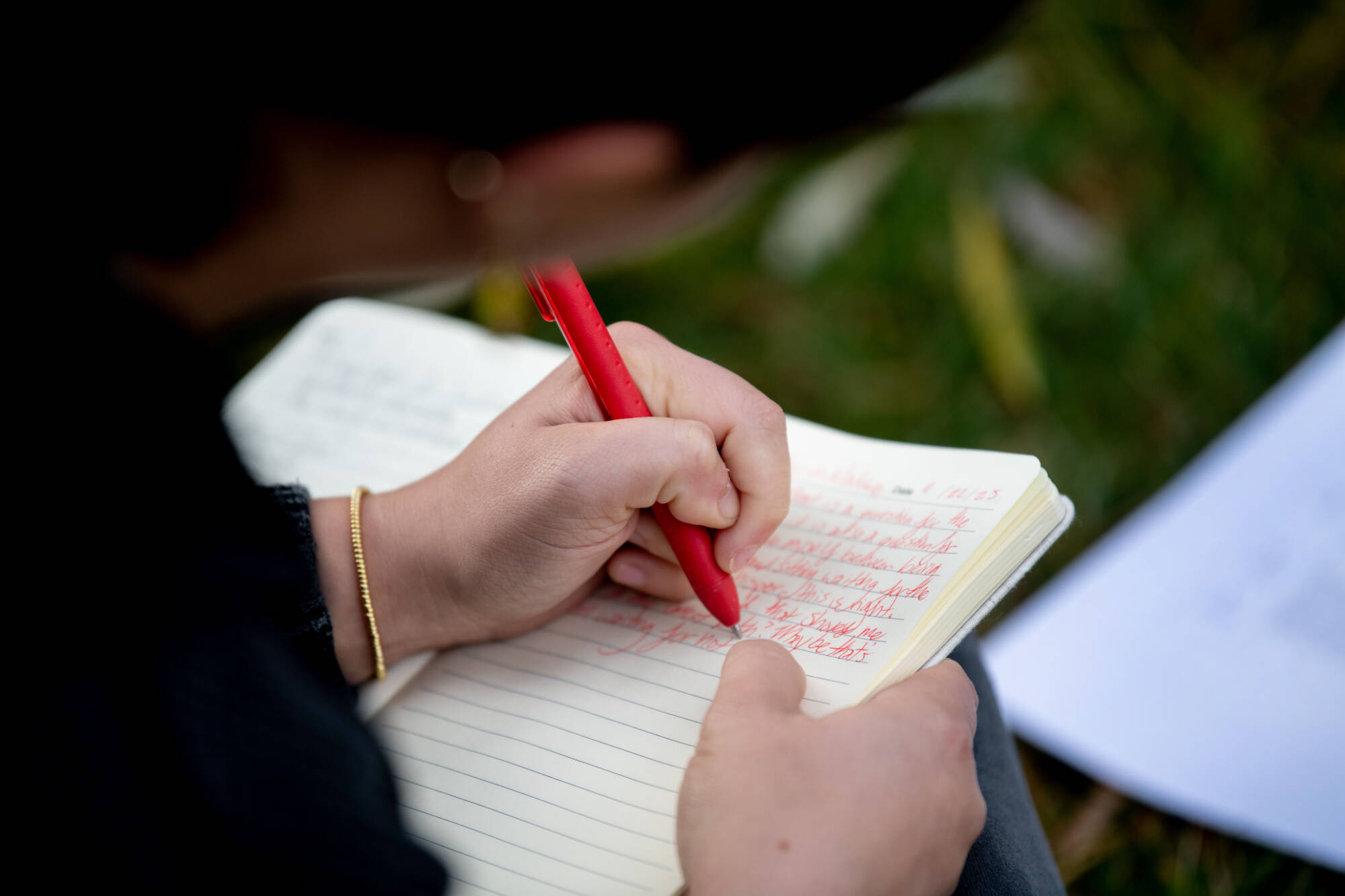 Student writing in notebook with red pen